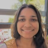 A person with long dark hair smiles at the camera