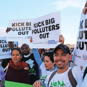 Multiple people at a rally holding signs that read Kick Big Polluters Out!
