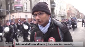 Sriram Madhusoodanan is interviewed by Democracy Now! at the Katowice climate march as riot police flood the background.