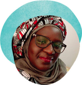 Portrait of Fatuo Diouf, a Black woman wearing dark-rimmed glasses and a headscarf patterned with red, white, gray, and black.