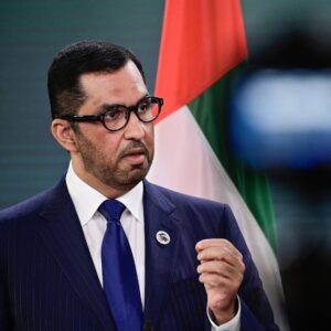 Sultan Al Jaber in a suit and tie with the United Arab Emirates flag in the background.