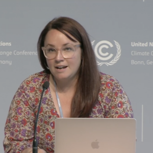 Rachel Rose Jackson on a UNFCCC Bonn panel organized by the Global Campaign to Demand Climate Justice. She speaks into a microphone with a computer in front of her.