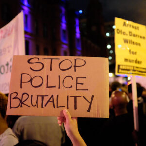 Scene at a night protest. The sign in the forefront reads "Stop Police Brutality"