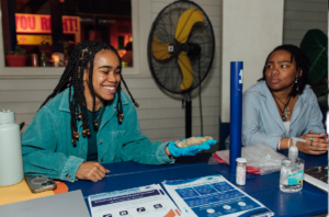 Two women sit at table and offer information about water lead testing.