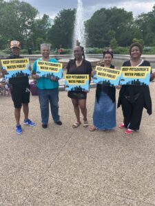 Five Black women stand together in front of a water foundation holding signs that read "Keep Pittsburgh's water public."