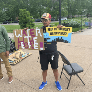 Activist in a park, holding signs that read: "water for the people" and "Keep Pittsburgh's water public"