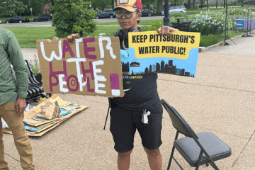 Activist in a park, holding signs that read: "water for the people" and "Keep Pittsburgh's water public"