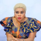 Zikora Ibeh, board member, wears a blue and orange top with intricate flower prints and gold hoop earrings.