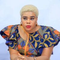 Zikora Ibeh, board member, wears a blue and orange top with intricate flower prints and gold hoop earrings.