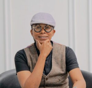 Portrait of Gabby Gray. She wears a gray cap and a vest, rests her chin in her hand, and smiles at the camera.