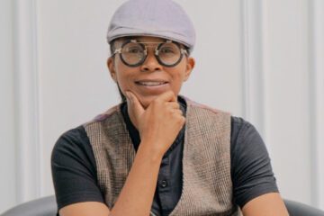 Portrait of Gabby Gray. She wears a gray cap and a vest, rests her chin in her hand, and smiles at the camera.