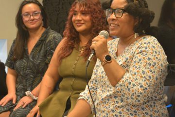 Three people engaging in a panel discussion, with the person closest to the camera talking into the microphone.