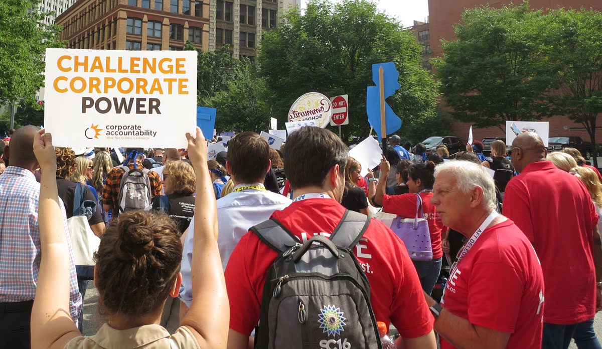 Activists holding signs that say 'Challenge Corporate Power'