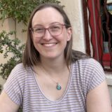 Portrait of Jamie Cerretti, Corporate Accountability board treasurer. Jamie is a white woman and she is wearing glasses and a striped shirt.