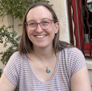 Portrait of Jamie Cerretti, Corporate Accountability board treasurer. Jamie is a white woman and she is wearing glasses and a striped shirt.